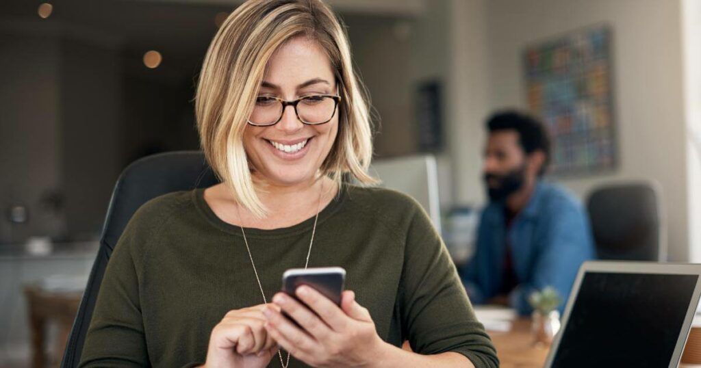 woman at desk smiling at phone