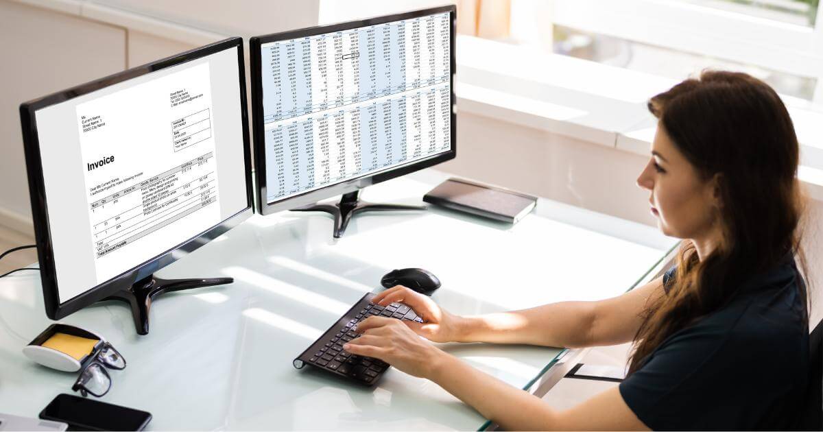 accountant in front of two monitors displaying invoices and spreadsheets