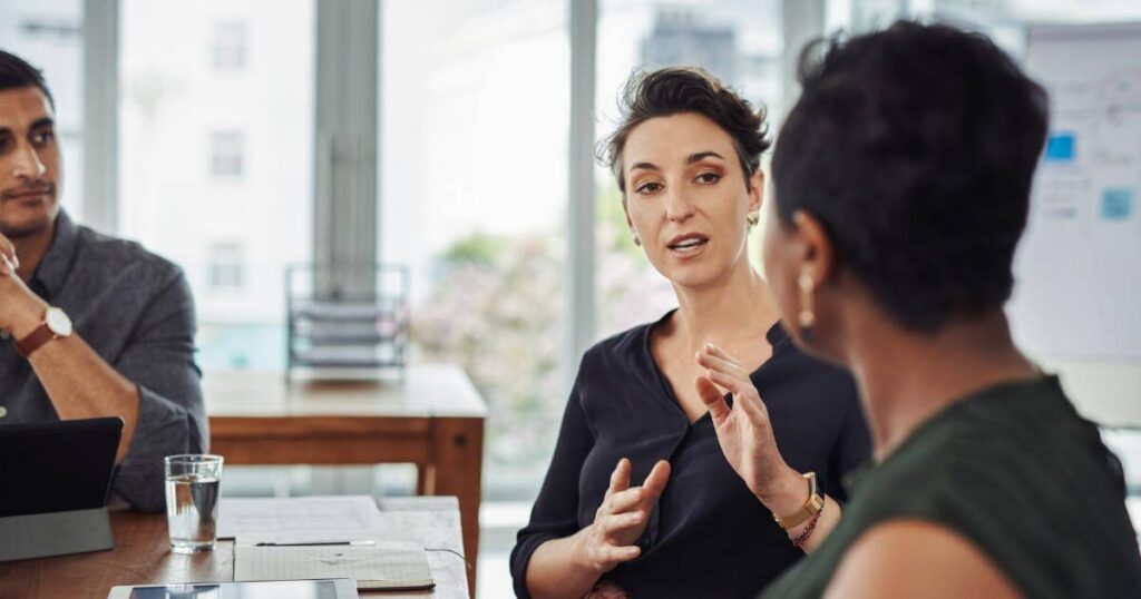 three professionals listening to coworker speak during meeting