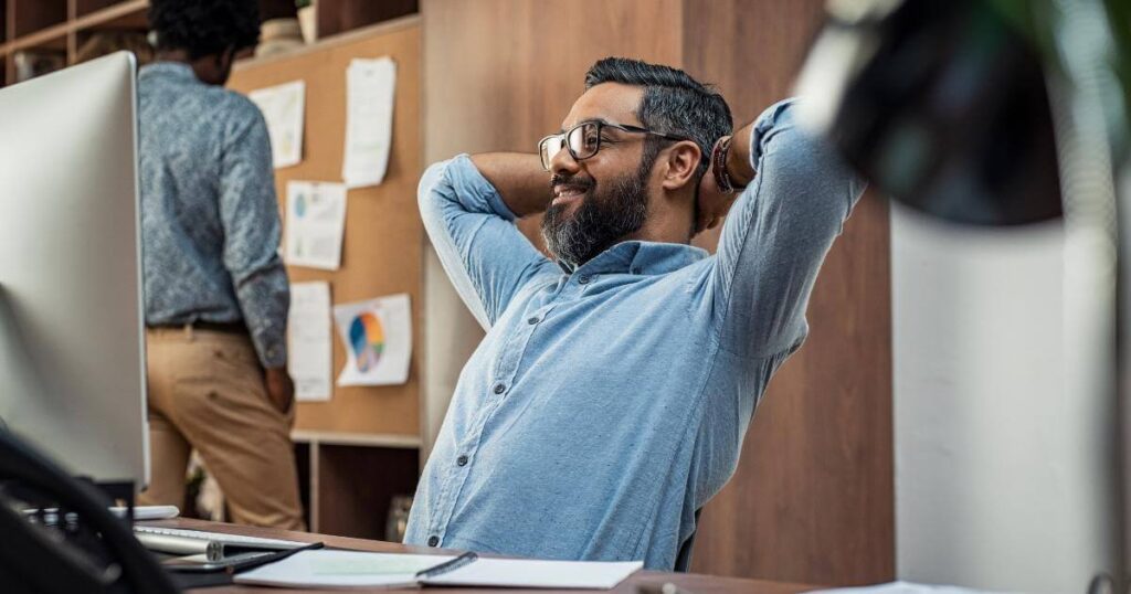 satisfied manager sitting at desk with arms behind his head